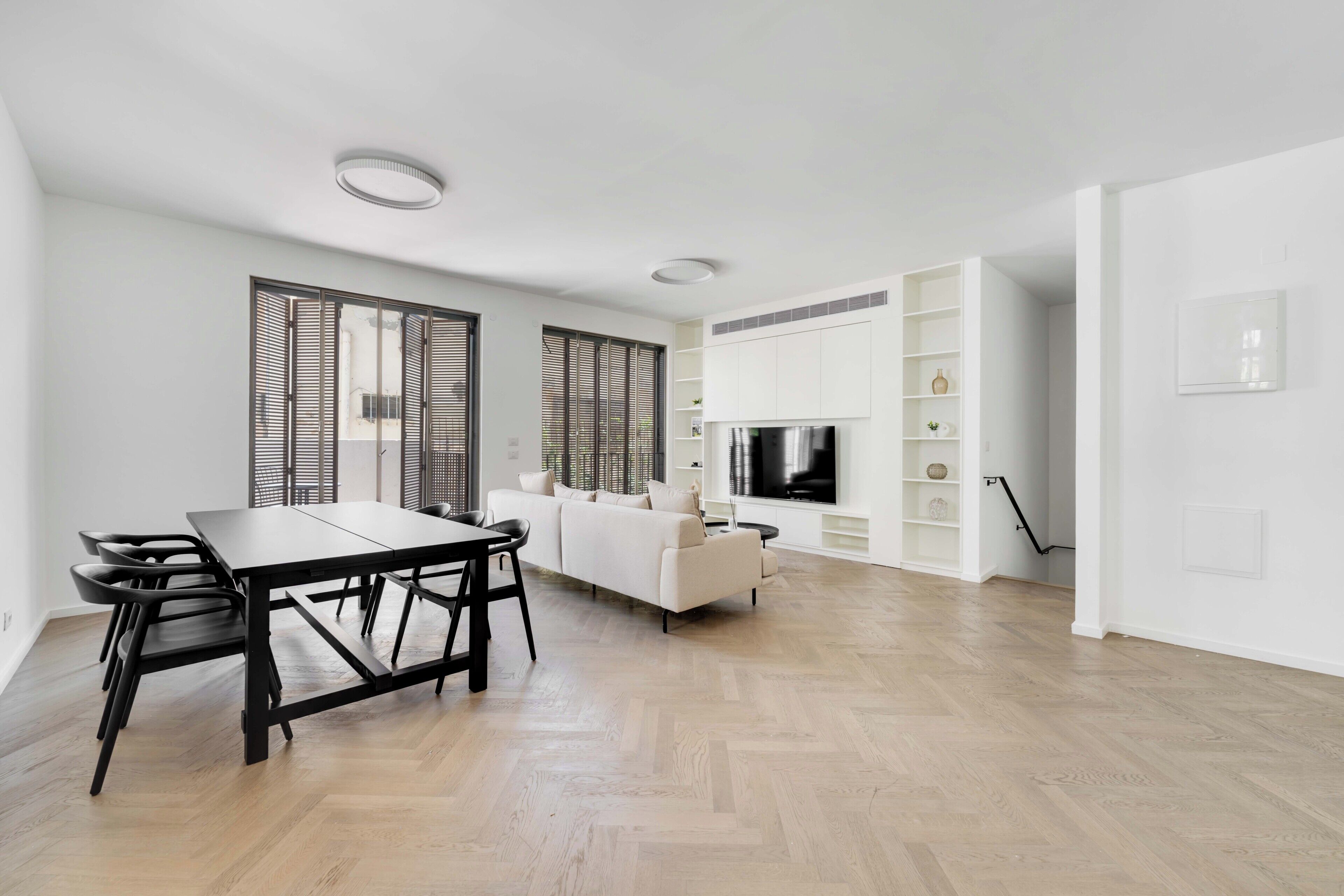 A modern living room with a dining area, a sofa, a TV, and built-in shelving.
