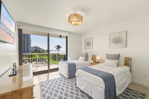 Habitación de hotel con dos camas, un balcón que ofrece vistas a la ciudad y un ventanal grande.