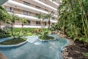 Un patio de hotel con fuente de agua, palmeras y un edificio de varios pisos con balcones.