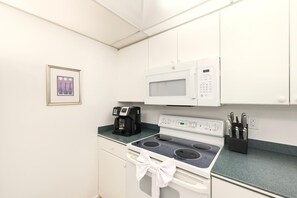 Une petite cuisine équipée d’un four à micro-ondes, d’une machine à café, d’une cuisinière et d’un bloc à couteaux.
