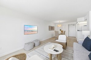 Ein modernes Wohnzimmer mit einem großen Flachbildfernseher, einem Essbereich mit Stühlen, einer Couch und einem kleinen Tisch mit Fernbedienung.