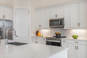 A modern kitchen with white cabinetry, stainless steel appliances, and a marble countertop. - Huge Waterfront Home | Six Ensuites, Pool & Spa (Marco Island)