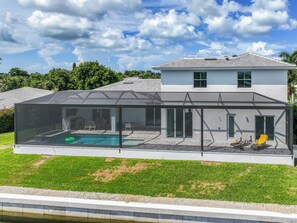 Una casa moderna con un patio con paredes de vidrio, una piscina y un césped cuidado.