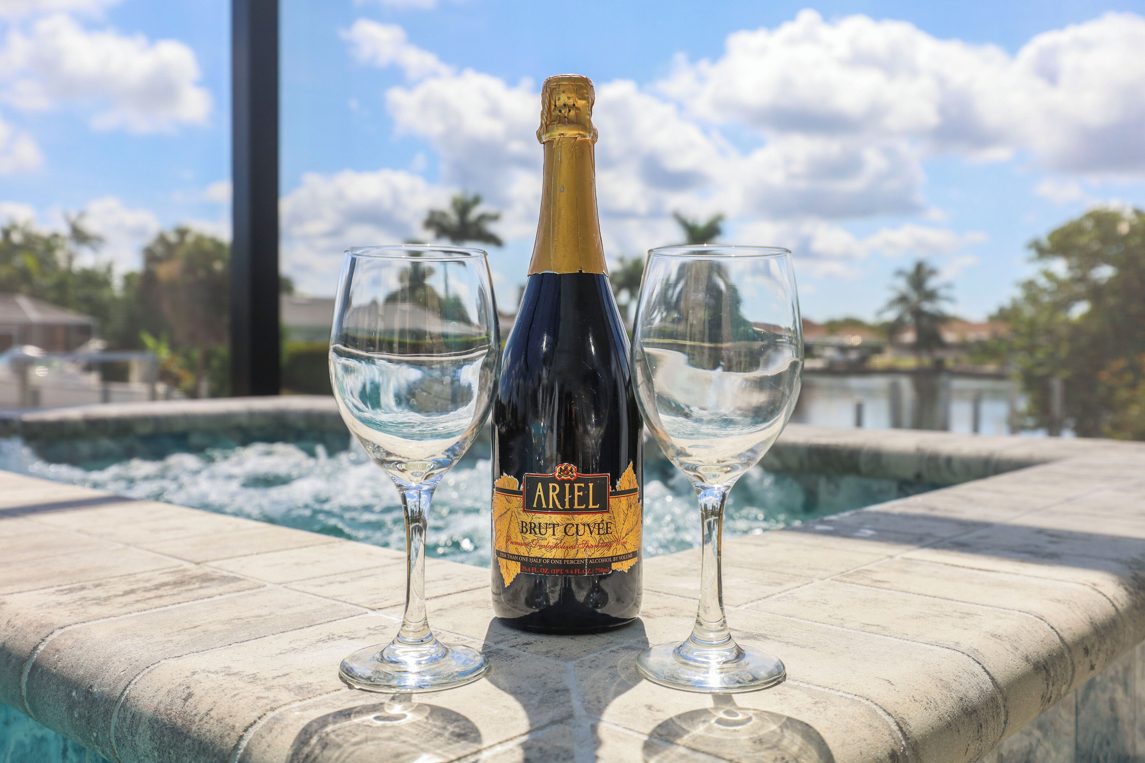 A bottle of Ariel Brut Cuvée champagne and two glasses on a poolside.