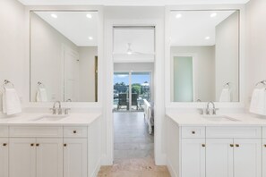 A modern bathroom with two sinks, large mirrors, and a view to a patio area. - Huge Waterfront Home | Six Ensuites, Pool & Spa (Marco Island)