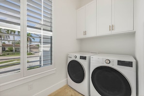 A laundry room with two front-loading washing machines, white cabinets above, and a window with blinds. - Huge Waterfront Home | Six Ensuites, Pool & Spa (Marco Island)