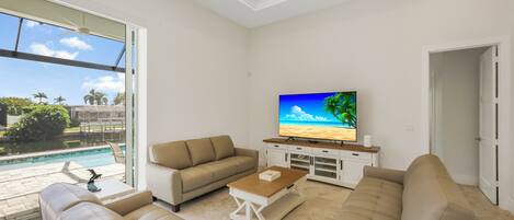Un salon moderne avec un grand téléviseur à écran plat, des canapés de couleur beige et une table basse.