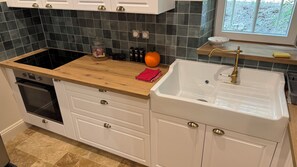 A kitchen with a wooden countertop, a white sink with a gold faucet, and a black stove.