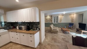 Une cuisine moderne avec des meubles blancs et un four à micro-ondes, un espace de vie avec un canapé et une table basse, et un mur d’accent en pierre.