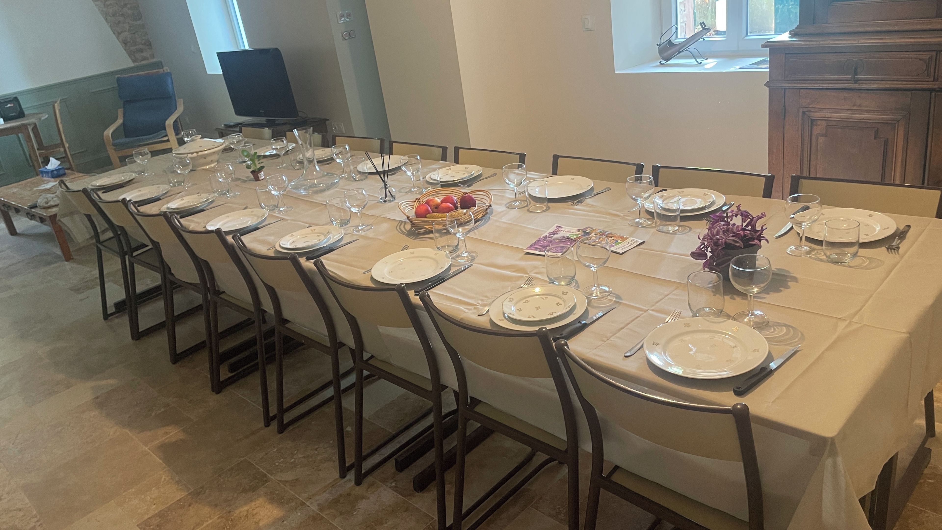 A dining table set for a meal with chairs, plates, cutlery, and a fruit basket.