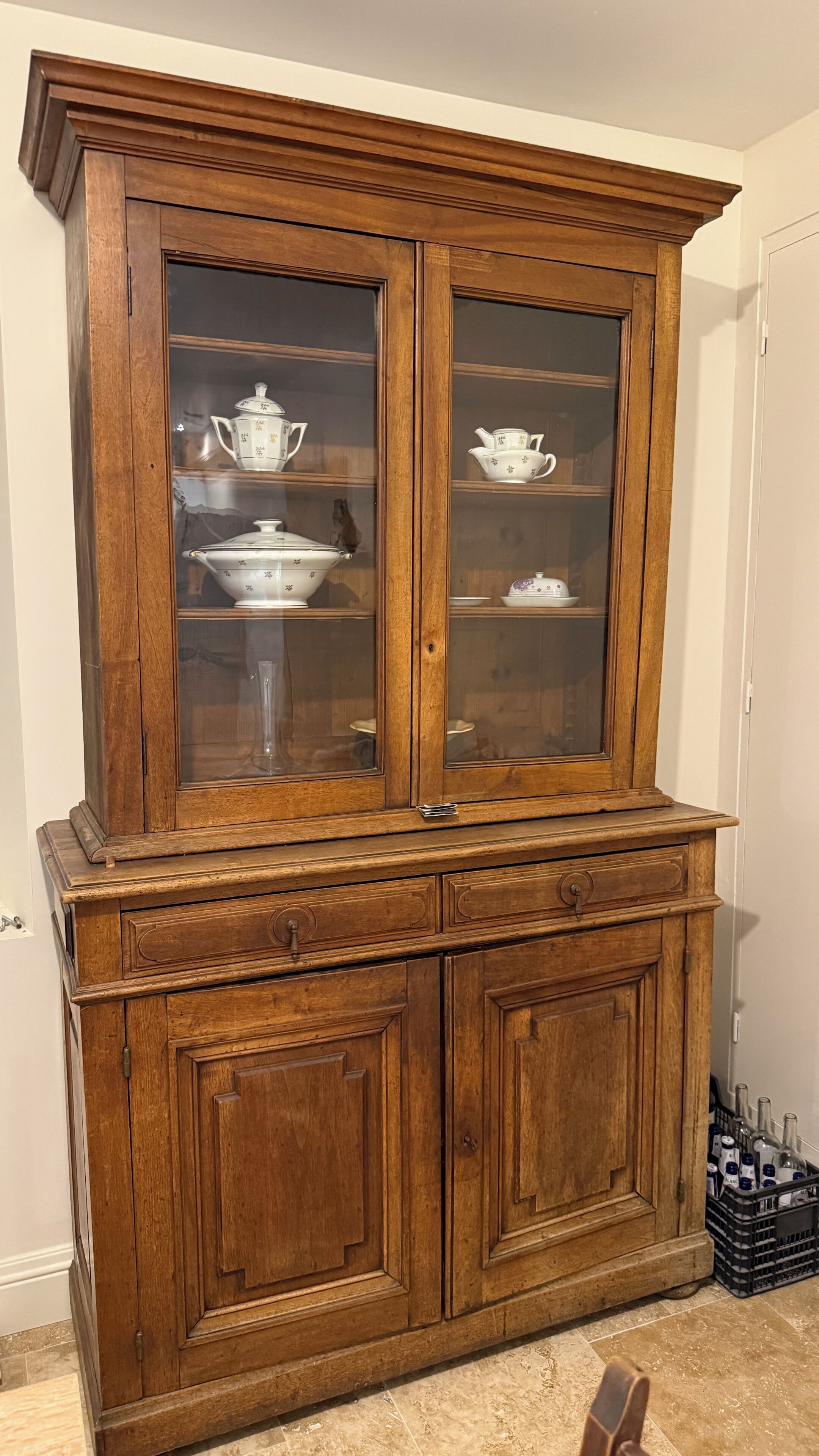 Un meuble en bois doté de portes en verre, de tiroirs et d’une étagère où sont disposés des objets en céramique blanche.