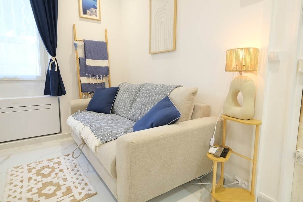 Ein modernes Wohnzimmer mit einem beigen Sofa, einem gemusterten Teppich, einer Lampe und einem an der Wand befestigten Regal.