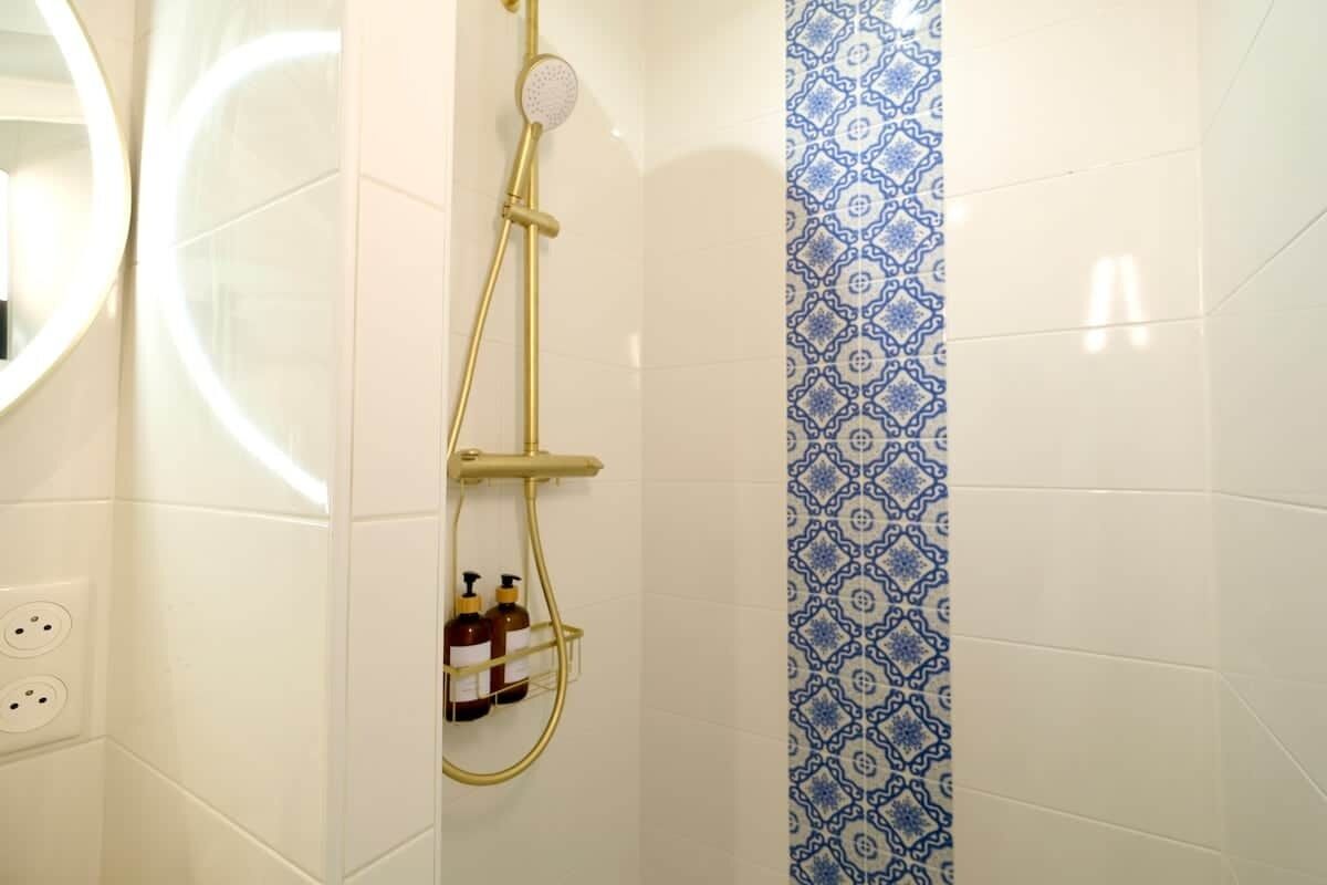 Una doccia con soffione flessibile, pannello comandi a parete e ripiano con articoli da toilette.