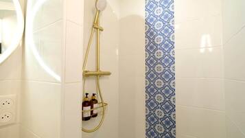 Una doccia con soffione flessibile, pannello comandi a parete e ripiano con articoli da toilette.