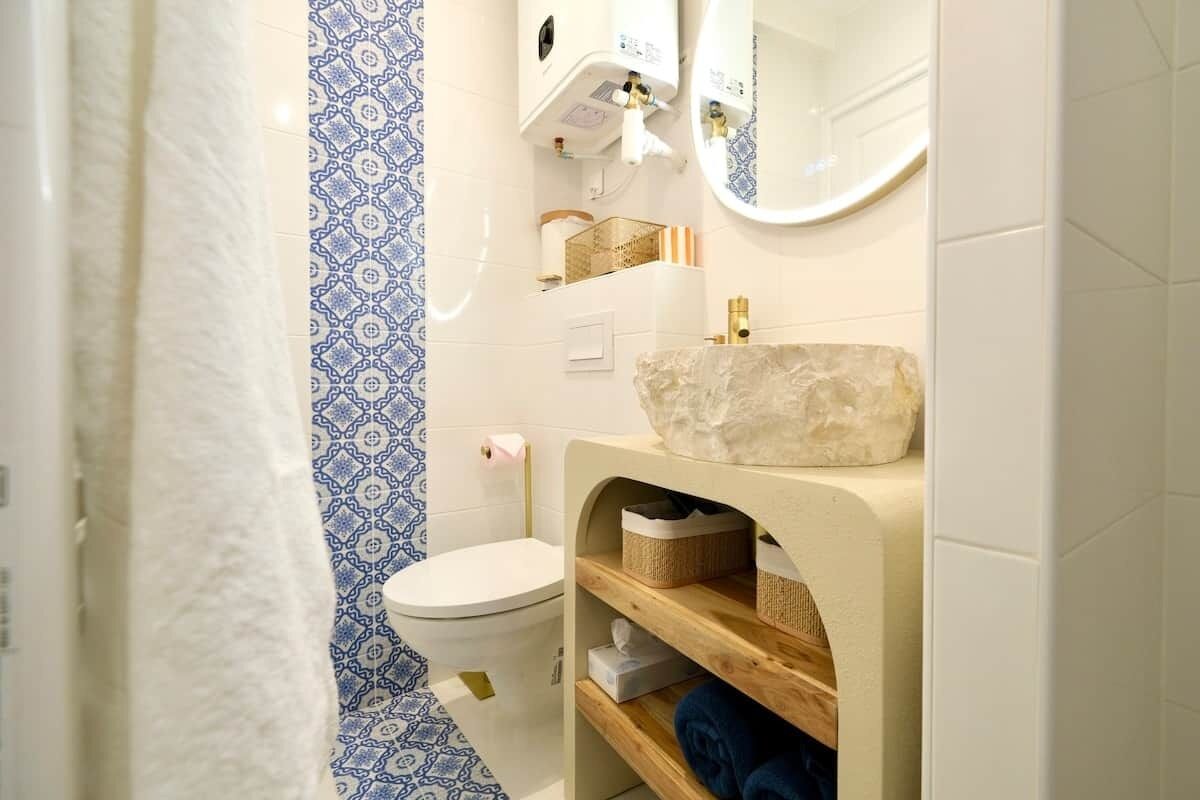 Un baño con inodoro, lavamanos de piedra, espejo y baldosas azules y blancas con diseño.