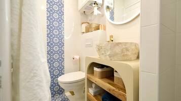 Un baño con inodoro, lavamanos de piedra, espejo y baldosas azules y blancas con diseño.