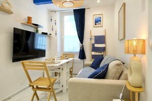 A modern living room with a flat-screen TV, a dining table, and a sofa with cushions. - Le Petit Santorin · Le Petit Santorin • Centre his (La Ciotat)