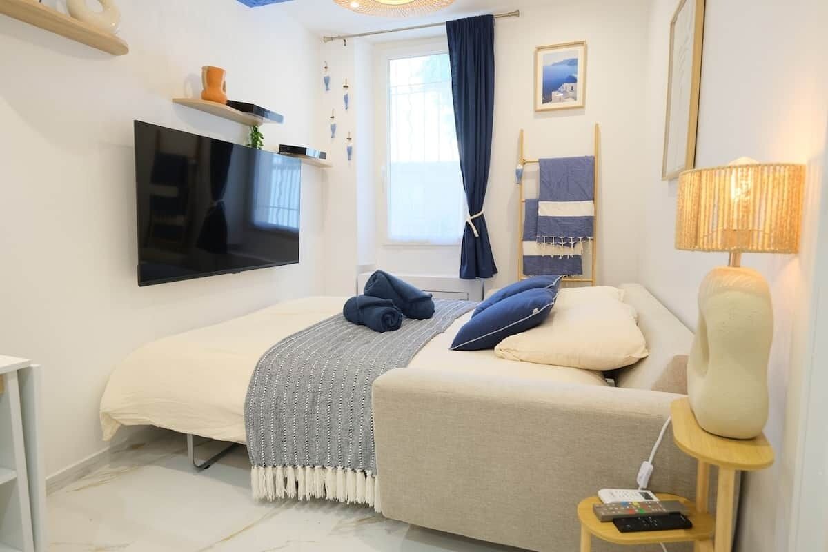 Een slaapkamer met een bed, een televisie, een nachtkastje met een lamp en een raam met gordijnen.