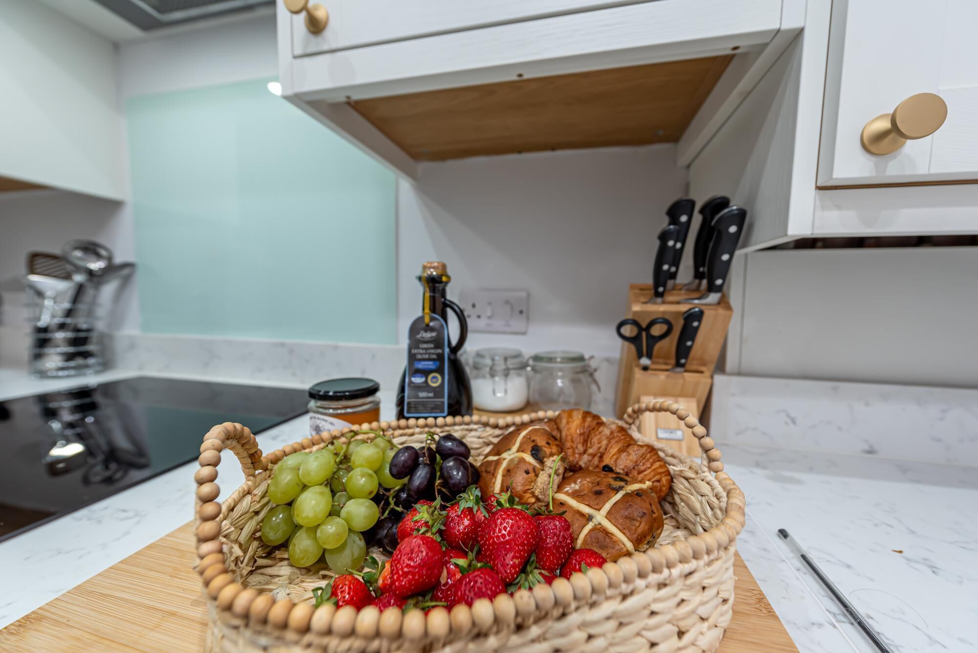 A kitchen counter with a wicker basket containing grapes, strawberries, and a croissant.