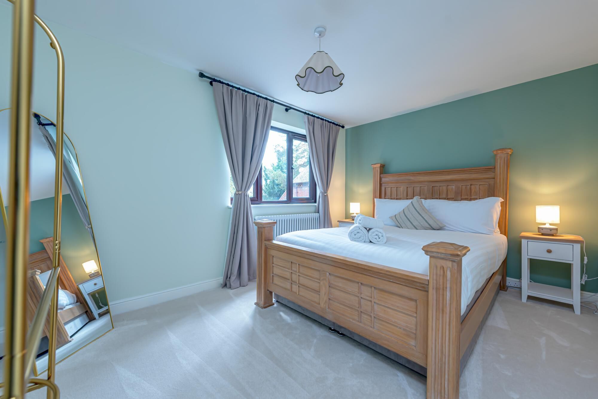 Un dormitorio con cama de madera, una mesita de noche, un espejo y una ventana con cortinas.