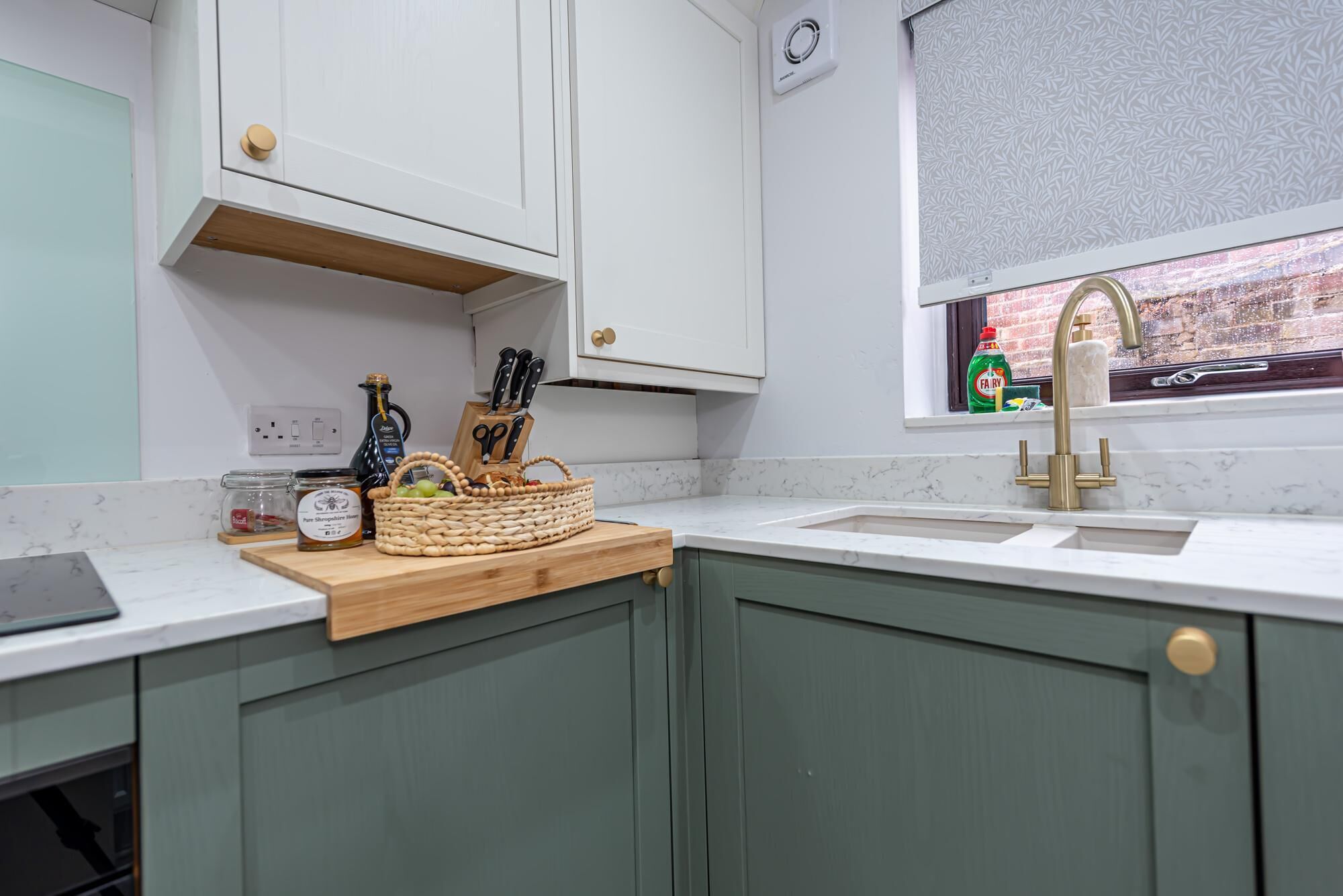 A kitchen with a marble countertop, a window with a view, and a sink with a gold faucet.