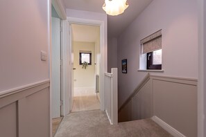 Ein Flur mit Teppichboden, einer Tür zu einem anderen Raum und einem Fenster mit Jalousie.