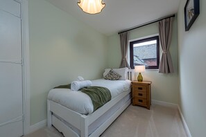 Ein Schlafzimmer mit Bett, Nachttisch, Lampe und einem Fenster mit Vorhängen.