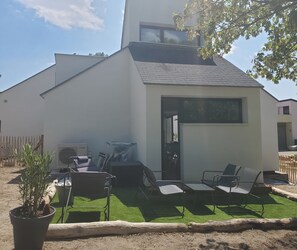 En modern byggnad med ett sluttande tak, ett takskyddat utomhusområde med sittplatser och en krukväxt.
