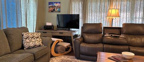 A living room with a sofa, a chair, a desk with a television, and a lamp.