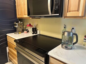 Une cuisine équipée d ’une plaque de cuisson à induction noire, d’un four à micro-ondes, de meubles en bois, d’une bouilloire en acier inoxydable et d’une machine à café.