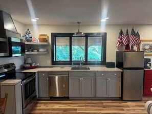 Una cocina moderna con electrodomésticos de acero inoxidable, lavavajillas y una ventana con vistas a zonas verdes.