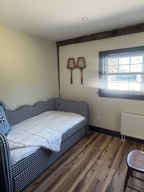 A room with a checkered bed, a radiator, a window with a view, and a chair.