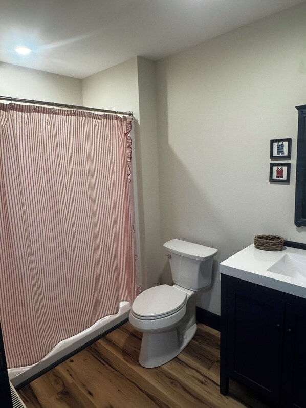 A bathroom with a shower curtain, toilet, and a sink with a dark cabinet.