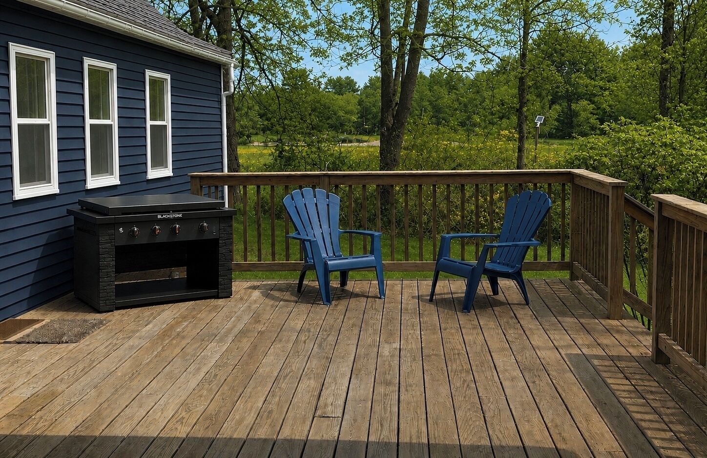 A deck with a grill, two Adirondack chairs, and a house with blue siding and white windows.