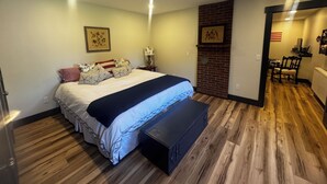 A bedroom with a bed, a bench, a fireplace, and a dining area.