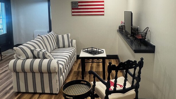 A living room with a striped sofa, a round table, a black chair, and an American flag on the wall.