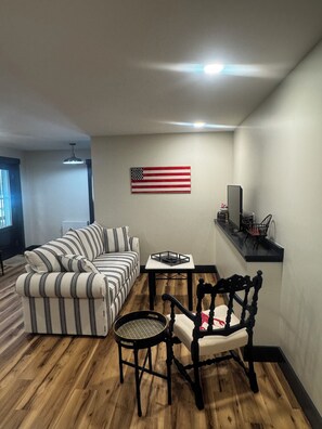 A living room with a striped sofa, a round table, a black chair, and an American flag on the wall.