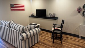 A living room with a striped sofa, a black chair, a TV on a shelf, and an American flag on the wall.