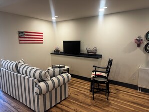 A living room with a striped sofa, a black chair, a TV on a shelf, and an American flag on the wall.