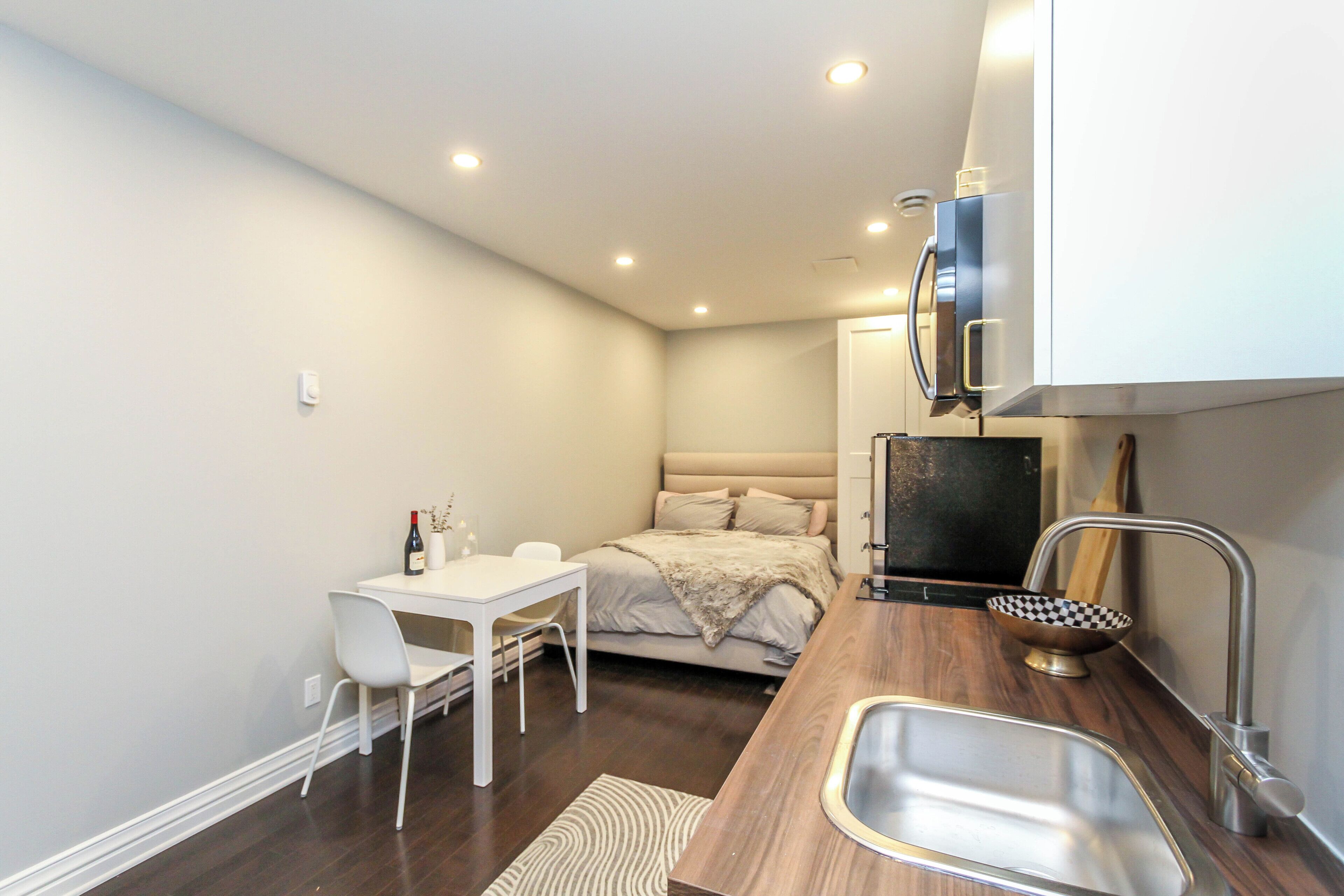 A compact bedroom with a bed, bedside table, and a small white desk with a chair.