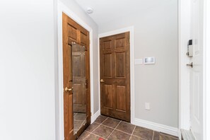 A hallway with two wooden doors, a white wall, and a tiled floor. - Bachelor Apartment in a perfect location of Ottawa (Ottawa)