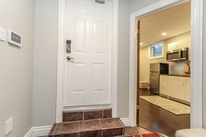A hallway with a white door, a digital clock, and a kitchen area with stainless steel appliances. - Bachelor Apartment in a perfect location of Ottawa (Ottawa)
