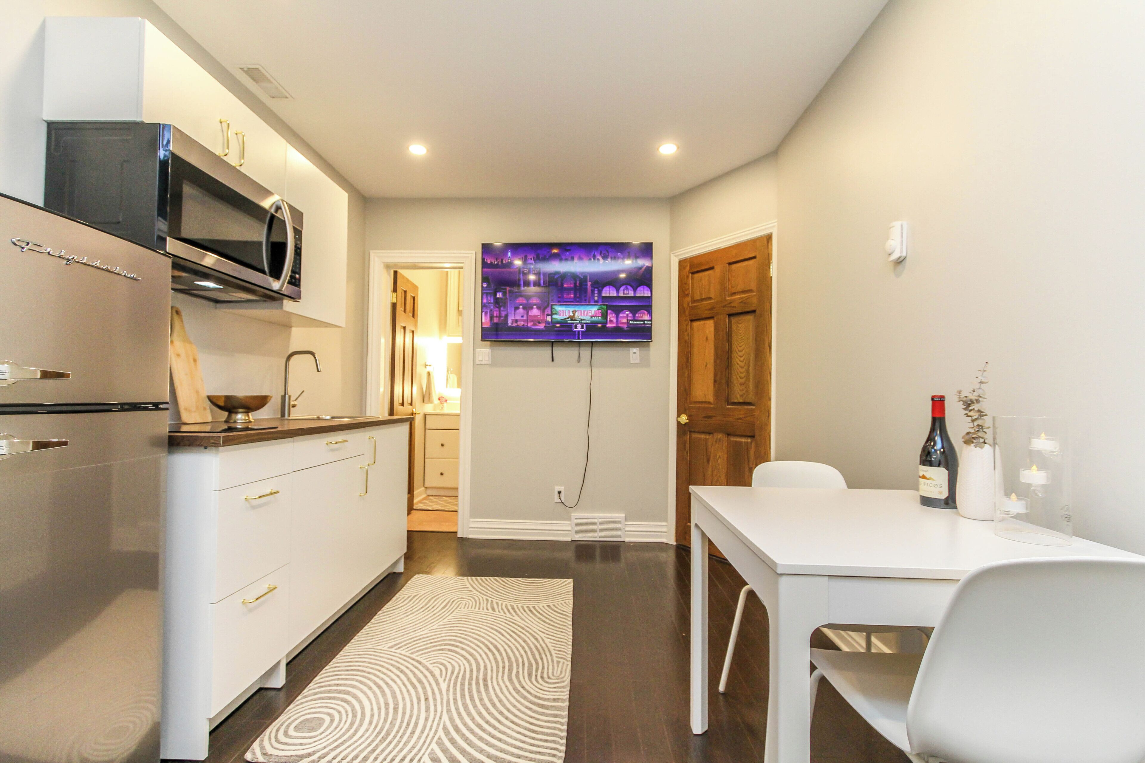 Una cucina moderna con forno a microonde integrato, un'area pranzo con tavolo e sedie bianche e un televisore fissato al muro.