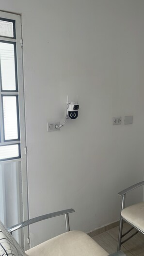 A room with a white wall, a security camera mounted on it, and a window with blinds.