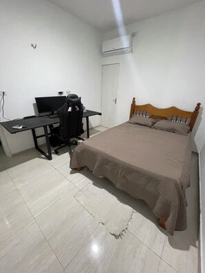 A bedroom with a bed, a desk with a computer, and an air conditioning unit.