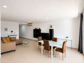 Ein modernes Wohnzimmer mit einer Couch, einem Glastisch und Stühlen. Ein Flachbildfernseher ist an der Wand befestigt.