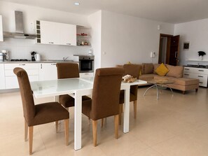 Eine moderne Küche mit weißen Schränken, einem Esstisch mit braunen Stühlen und einer Wohnbereich mit einer Couch und einem Couchtisch.