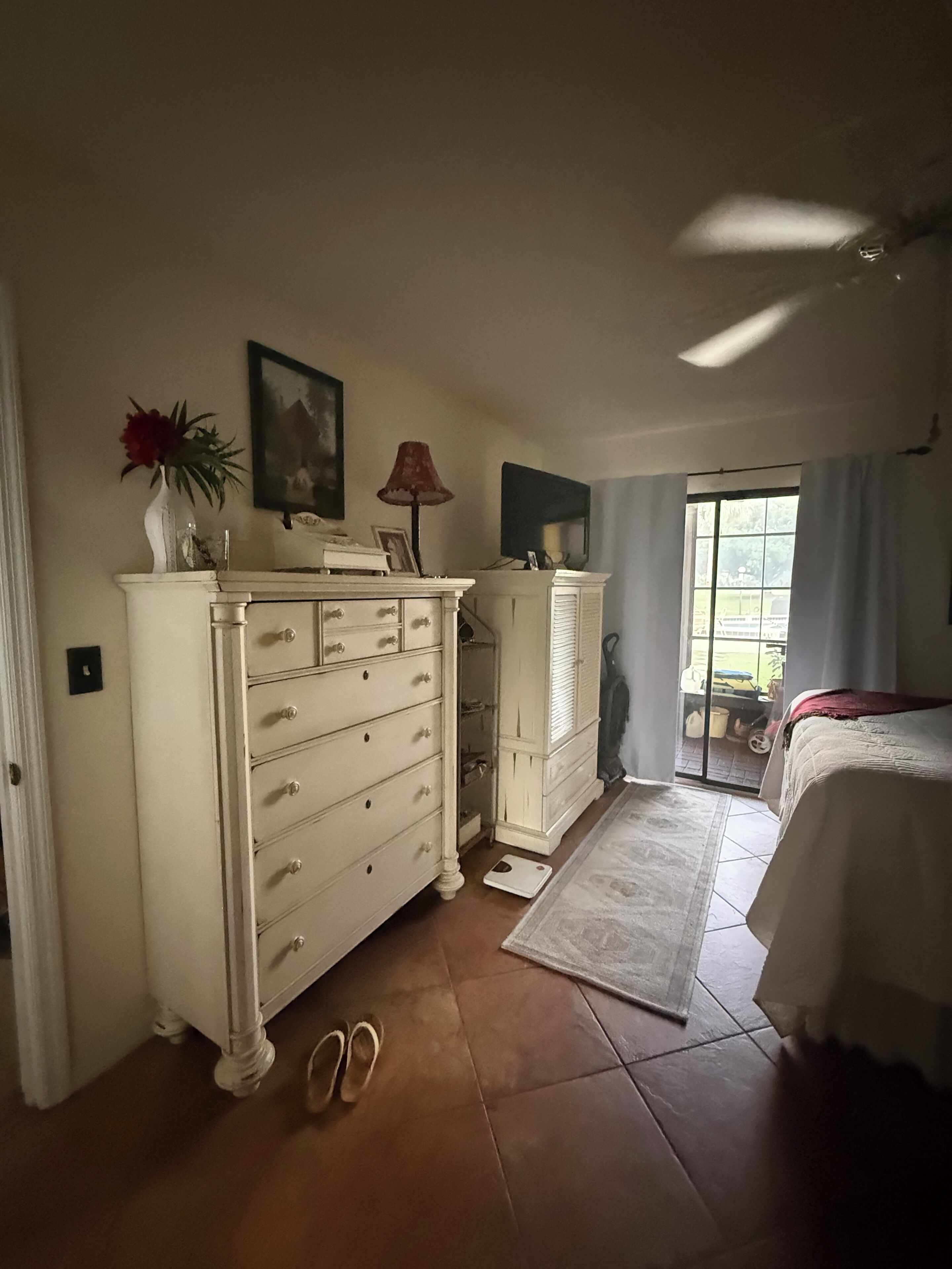 Une chambre à coucher avec un lit, une commode, une lampe et une fenêtre avec des rideaux.