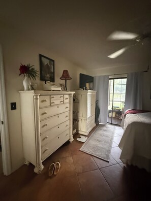 Une chambre à coucher avec un lit, une commode, une lampe et une fenêtre avec des rideaux.