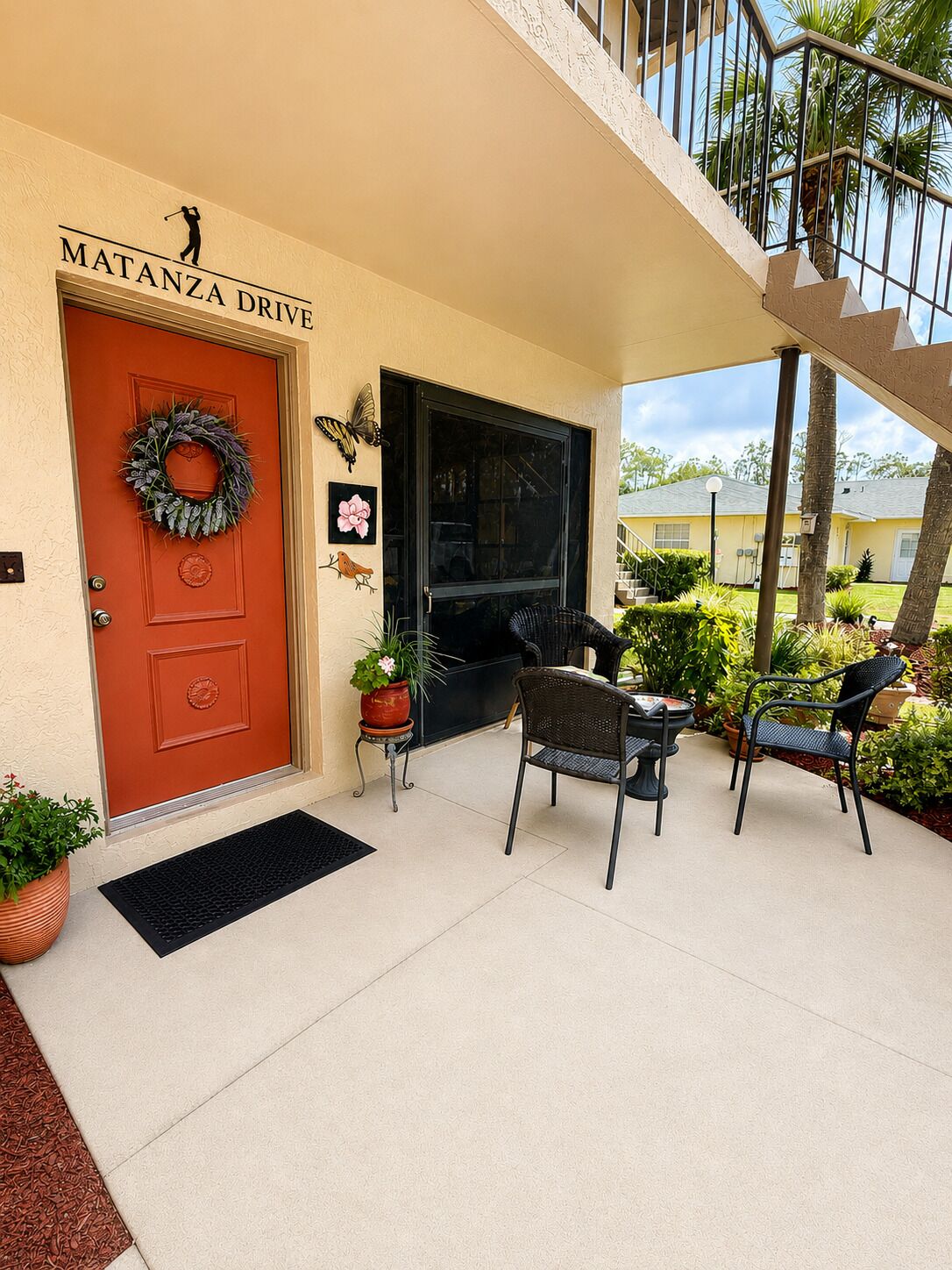 Une entrée de maison avec une porte rouge, une guirlande décorative et un espace patio aménagé avec du mobilier d’extérieur.